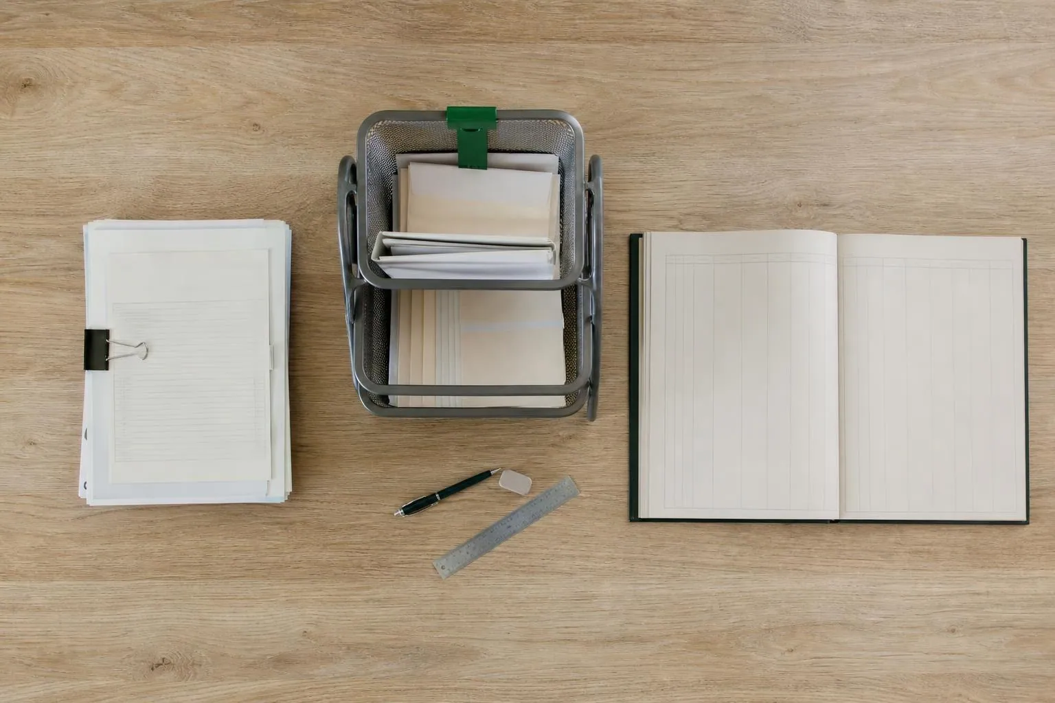 Vue de dessus d’une table de réunion où sont posés côte à côte une pile de feuilles imprimées, un bac à courrier et un registre relié